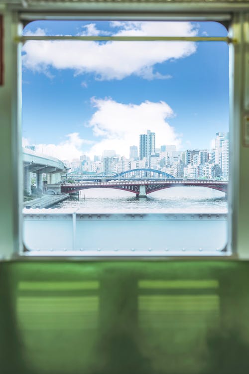 View of Bridge and City Buildings Under Blue Sky from a Glass Window