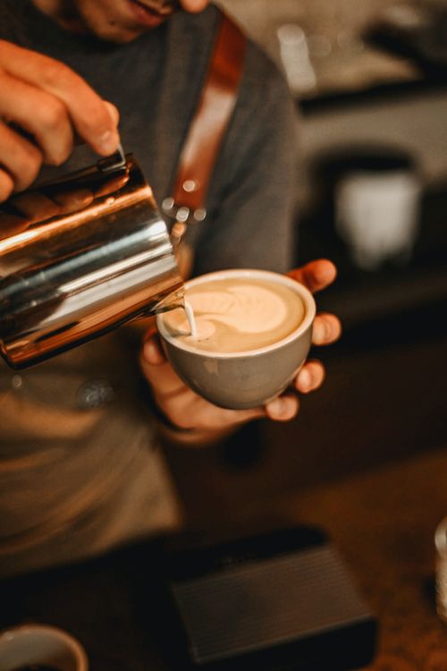Free A barista skillfully pours latte art into a freshly brewed cappuccino. Stock Photo