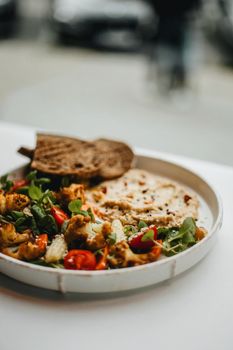 A vibrant vegan salad with roasted vegetables and bread in a cozy setting.