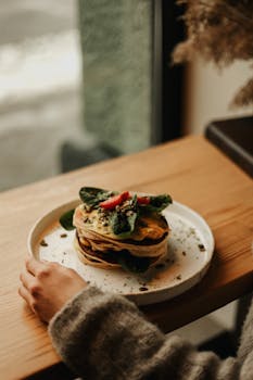 A stack of homemade pancakes topped with fresh vegetables on a wooden table.