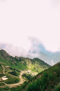 Mountain view with lush green slopes, winding trails, and misty clouds.