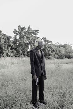 Black and white of full length of young African American male wearing jacket and trousers with helmet on head and transparent protective shield on face standing in grassy field