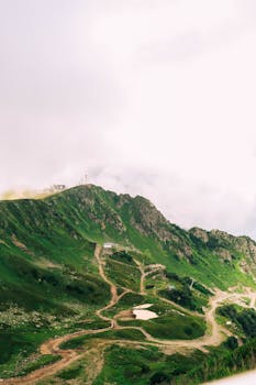 Scenic aerial view of a green mountain landscape with winding trails against a bright sky.