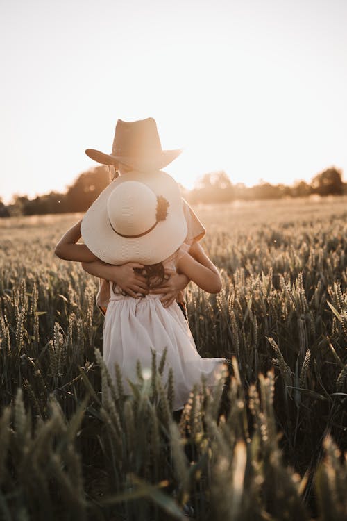 Unrecognizable boy and girl in hats hugging each other in field with cereal grass at sundown in countryside