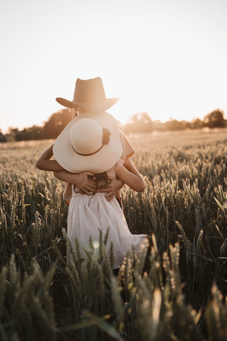 Kids Embracing On Grassy Field At Sunset