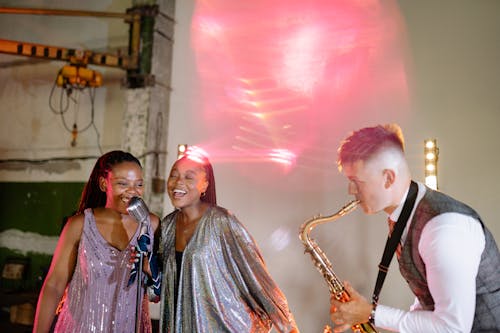 Free A Pair of Women Singing with a Microphone Beside a Man Playing the Saxophone  Stock Photo