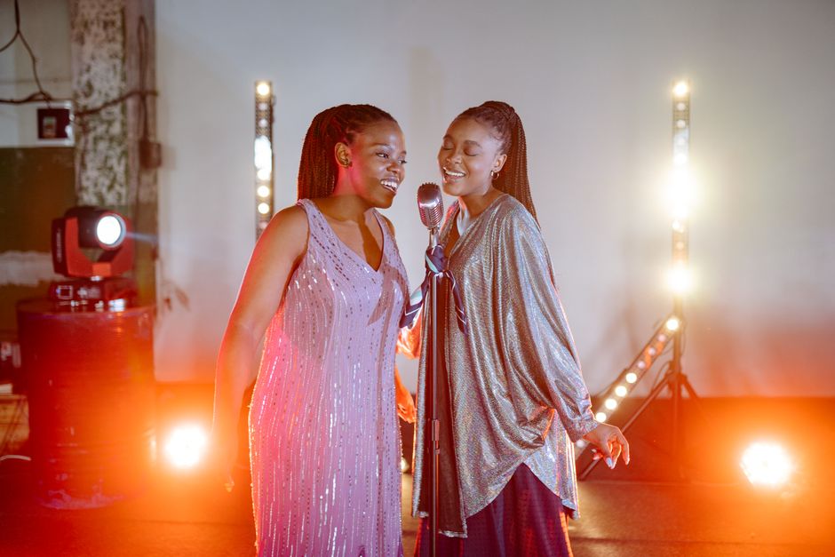 Two women performing a duet on stage under bright spotlights, singing passionately.