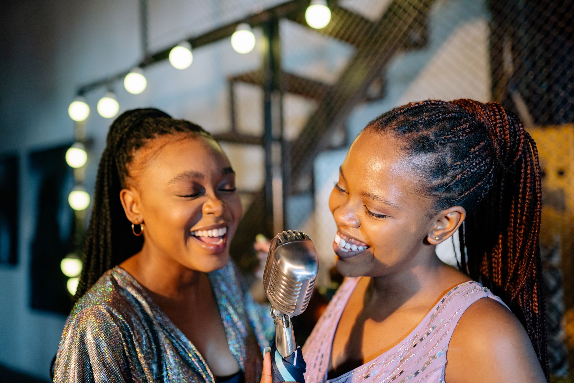 Two African American women joyfully singing with a vintage microphone indoors.