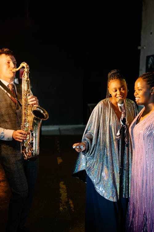 Women Singing Beside a Man Playing the Saxophone