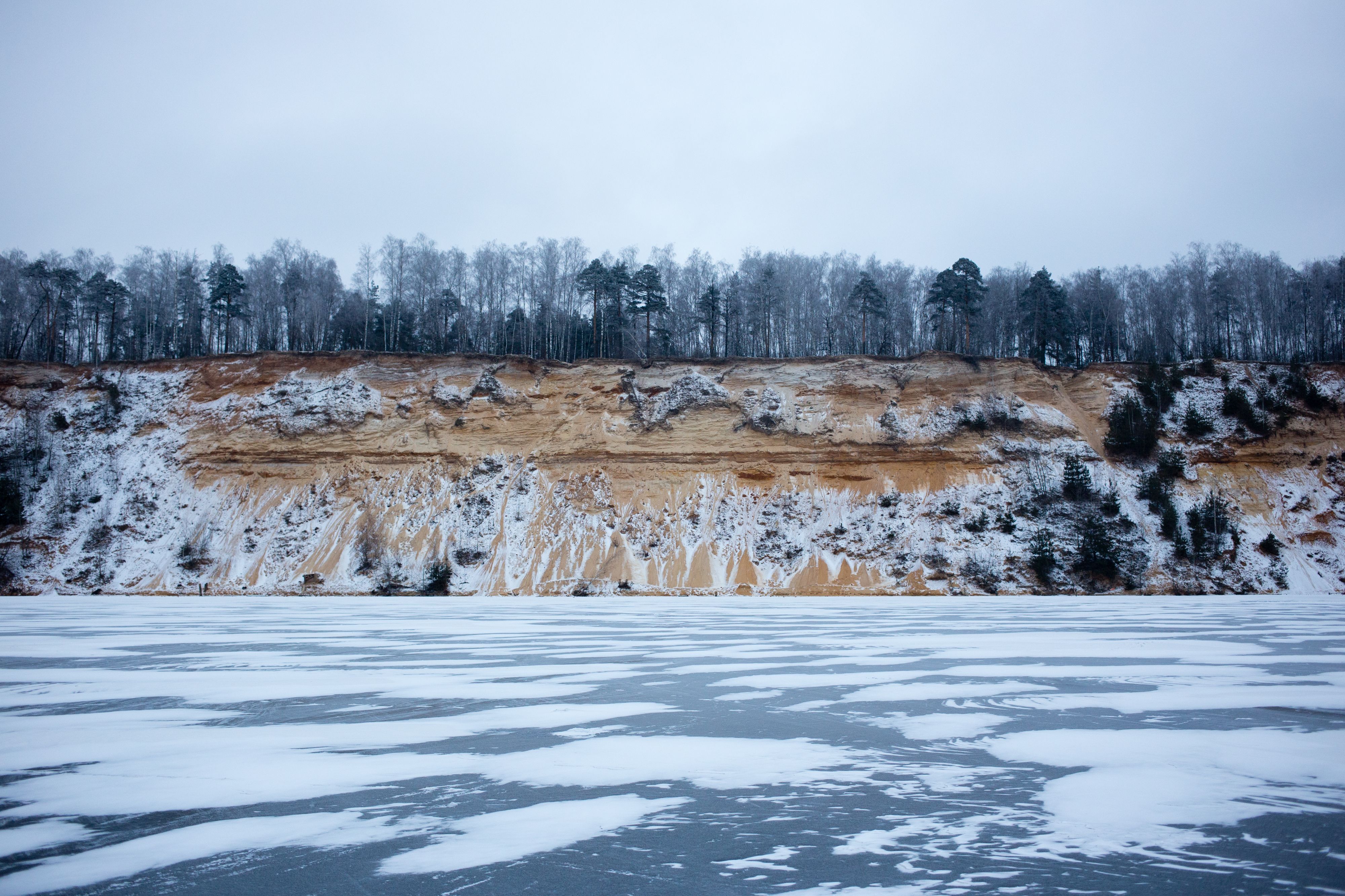 Scenic winter landscape of the frozen Dzerzhinskiy quarry with snow-covered trees and cliffs.