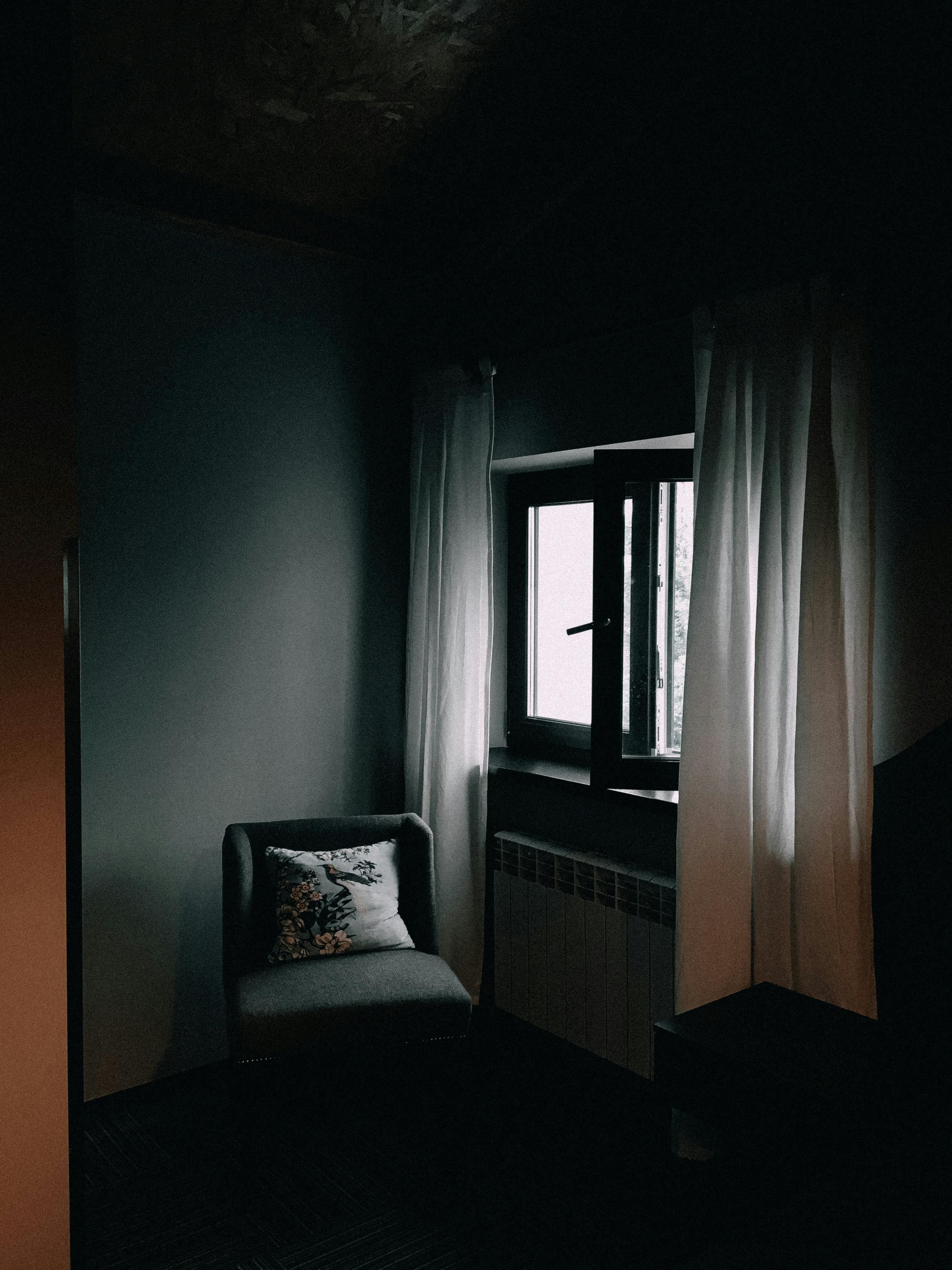 Free A dimly lit corner featuring a cozy armchair near an open window, creating a relaxed atmosphere. Stock Photo