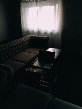 Dimly lit living room featuring a sofa and opened laptop on a table by a window.
