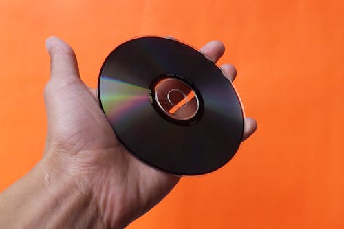Fotobanka s bezplatnými fotkami na tému kompaktný disk, orange_background, ruka