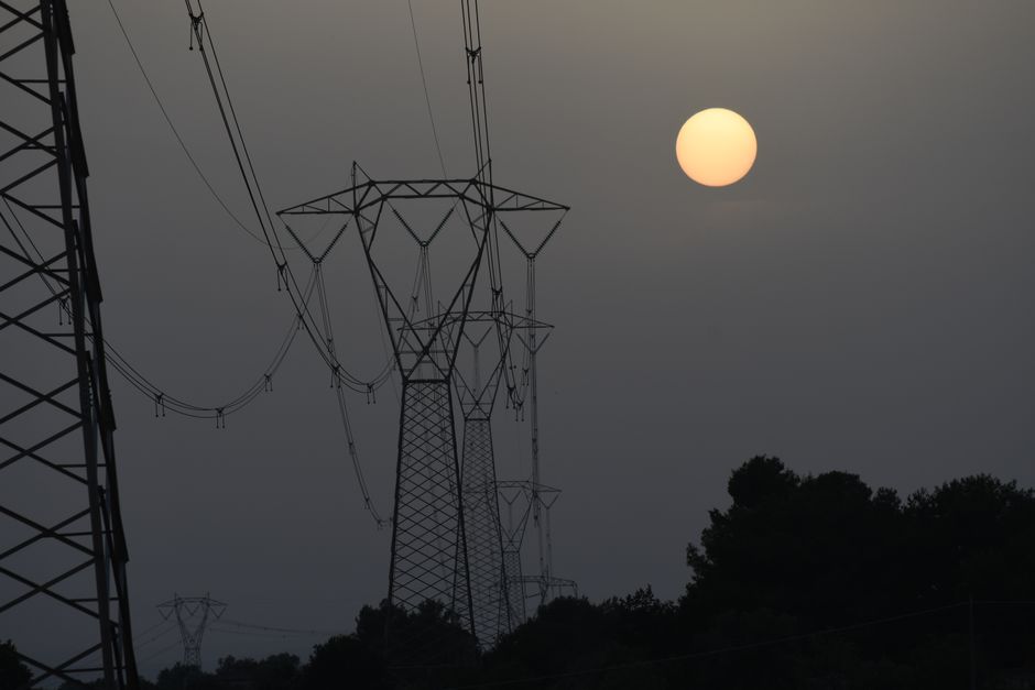 Transmission towers silhouetted against a setting sun, creating an industrial sunset scene.