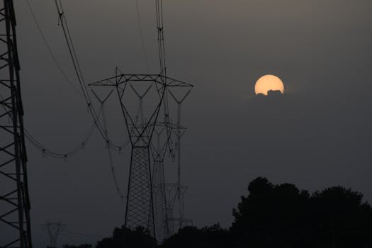 Silhouetted utility poles and power lines against a moody sunset sky.