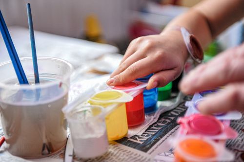 Free A close-up of a child painting with colorful acrylic paints and brushes indoors. Stock Photo