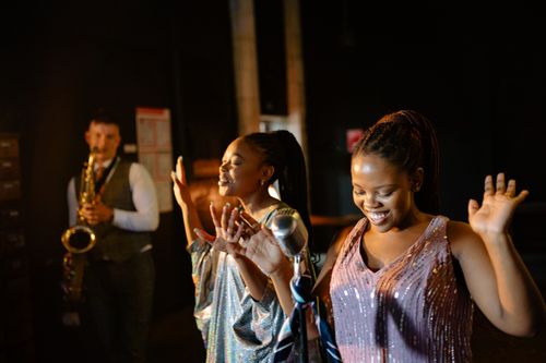 Free Black women singing energetically with a saxophone player in a lively jazz performance. Stock Photo