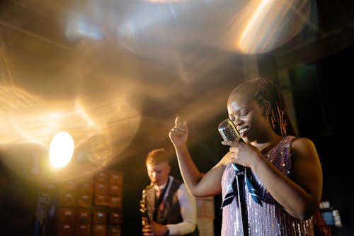 A Woman Singing Holding a Microphone Near a Man Playing the Saxophone