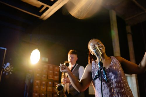 Free Woman singing energetically with microphone and band in cozy indoor setting. Stock Photo