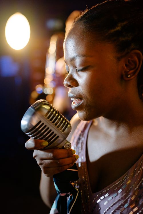 Free African American woman singing passionately on stage with vintage microphone. Stock Photo
