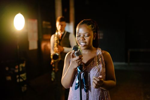 Free A captivating jazz performance featuring a female singer and saxophonist on stage under warm spotlight. Stock Photo