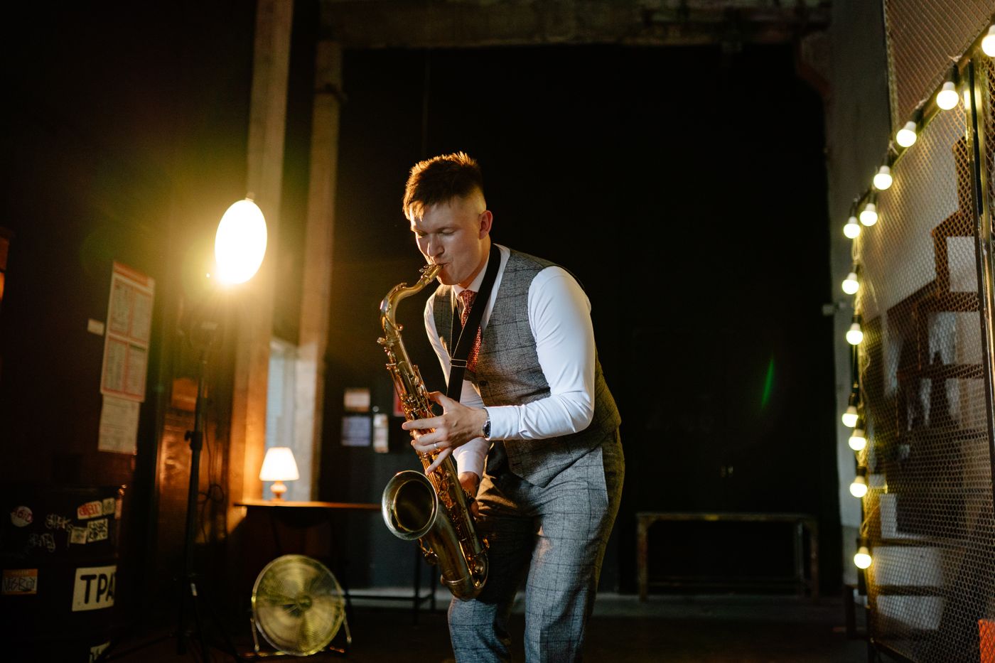 A saxophonist performing in a dim room lit by warm lamps