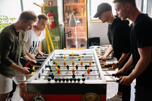 Free Four young men intensely playing foosball in a lively indoor space. Stock Photo