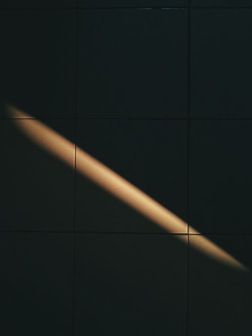 Free Abstract shot of light and shadow creating a diagonal pattern on dark tiled wall. Minimalist and artistic composition. Stock Photo