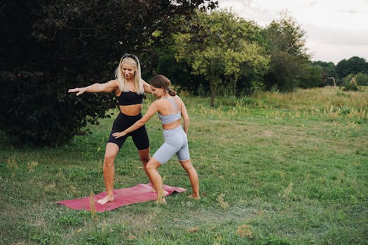Two women practicing yoga outdoors on a mat surrounded by greenery.