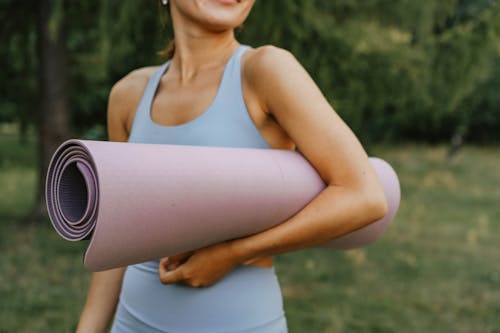 A Person in Blue Tank Top Holding Rolled Yoga Mat