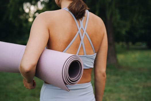 Back view of a woman holding a yoga mat in a peaceful outdoor setting.