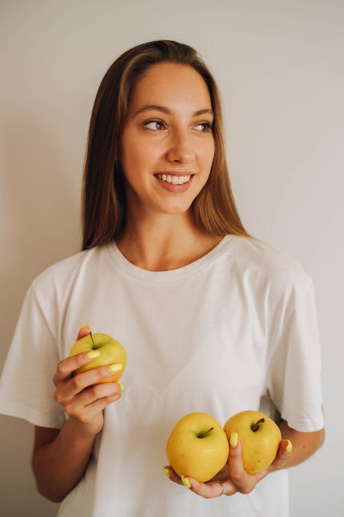 Woman in White T-shirt Holding Yellow Apples and Smiling