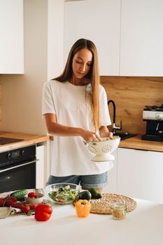 Woman rinsing vegetables in a modern kitchen, promoting healthy eating.
