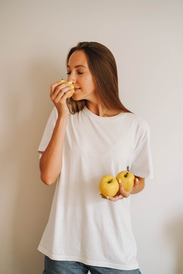 A Woman Wearing A White Shirt Smelling A Pear