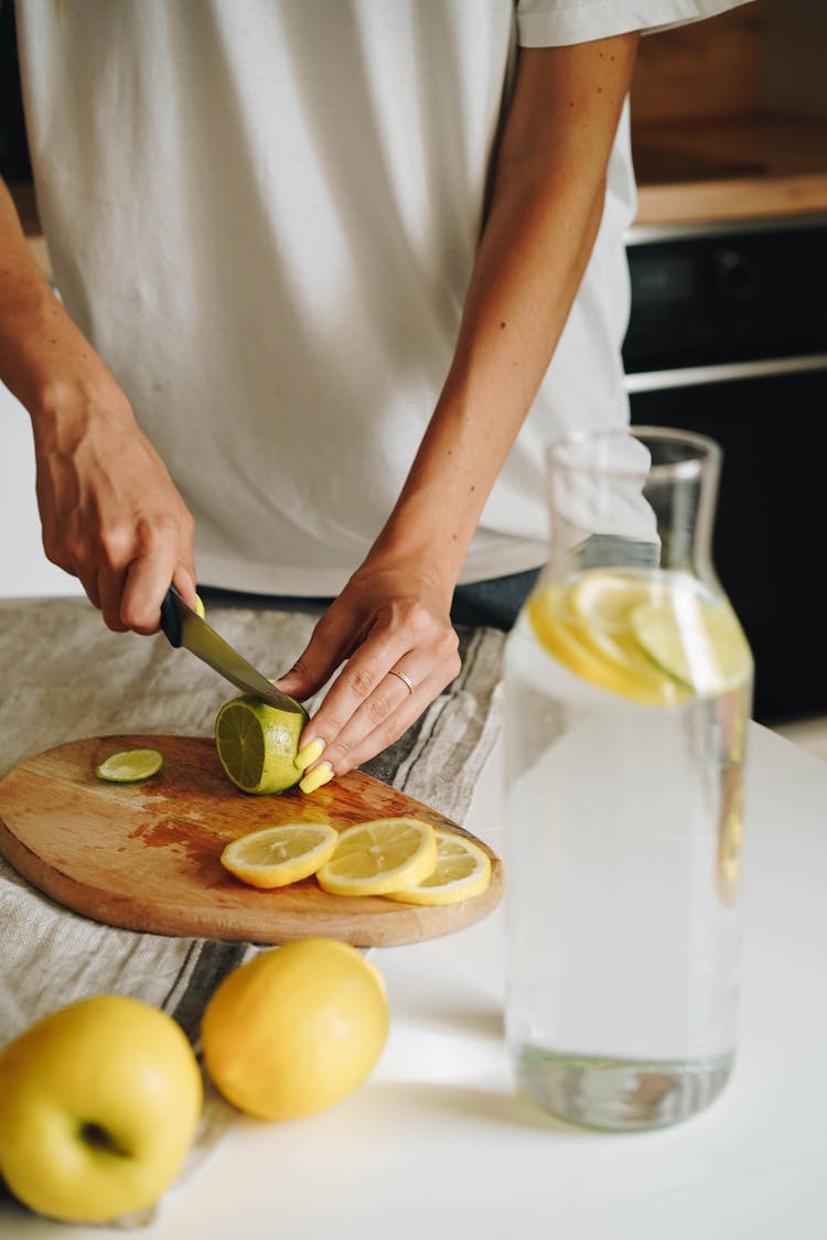 Person Slicing Lime On Brown Wooden Chopping Board