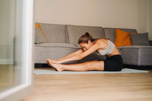 Free Woman in activewear stretching on yoga mat at home, promoting a healthy lifestyle. Stock Photo