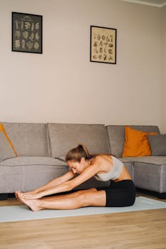 Young woman performing seated stretch on yoga mat in cozy living room setting.