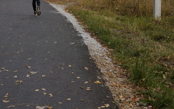 A woman in a blue jacket jogging through a tranquil autumn forest path with fallen leaves.
