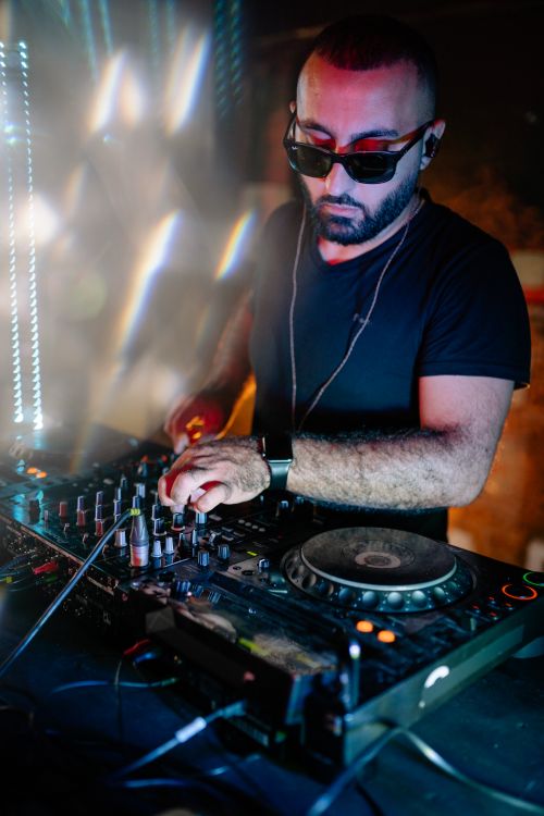 Free A DJ wearing sunglasses mixing music on turntables during a vibrant nightclub party. Stock Photo