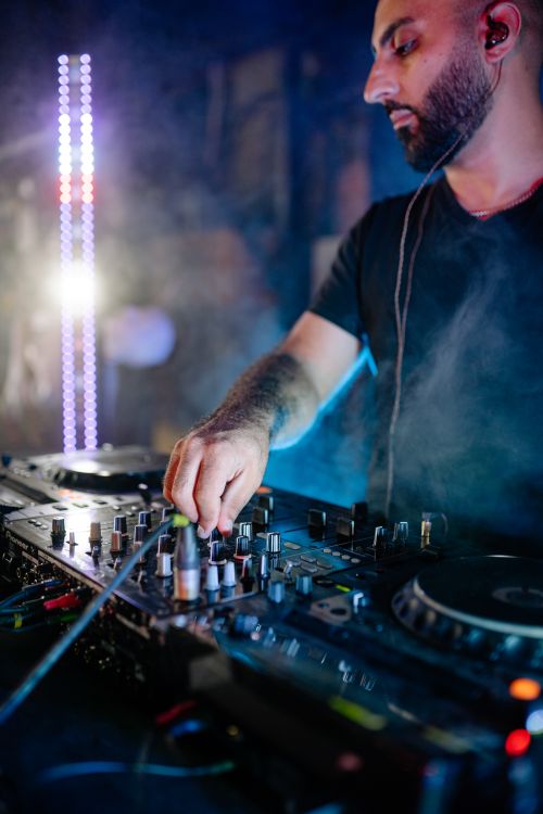 Free DJ focused on mixing tracks in a vibrant nightclub atmosphere with lights and smoke. Stock Photo