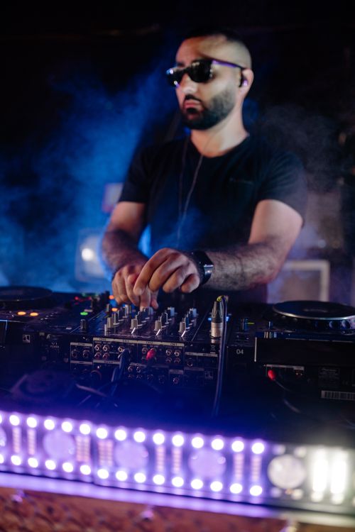 Free DJ performing live with mixing equipment, turntables, and vibrant lights in a smoky club atmosphere. Stock Photo