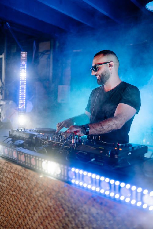 Free Energetic DJ playing music at a nightclub with vibrant lighting and smoke effects. Stock Photo