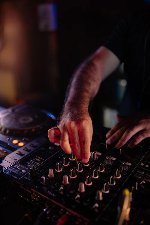 Free Close-up of a DJ's hands adjusting an audio mixer in a dimly lit club scene. Stock Photo