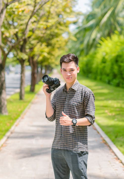 Free A Man Holding a Camera While Standing on the Sidewalk  Stock Photo