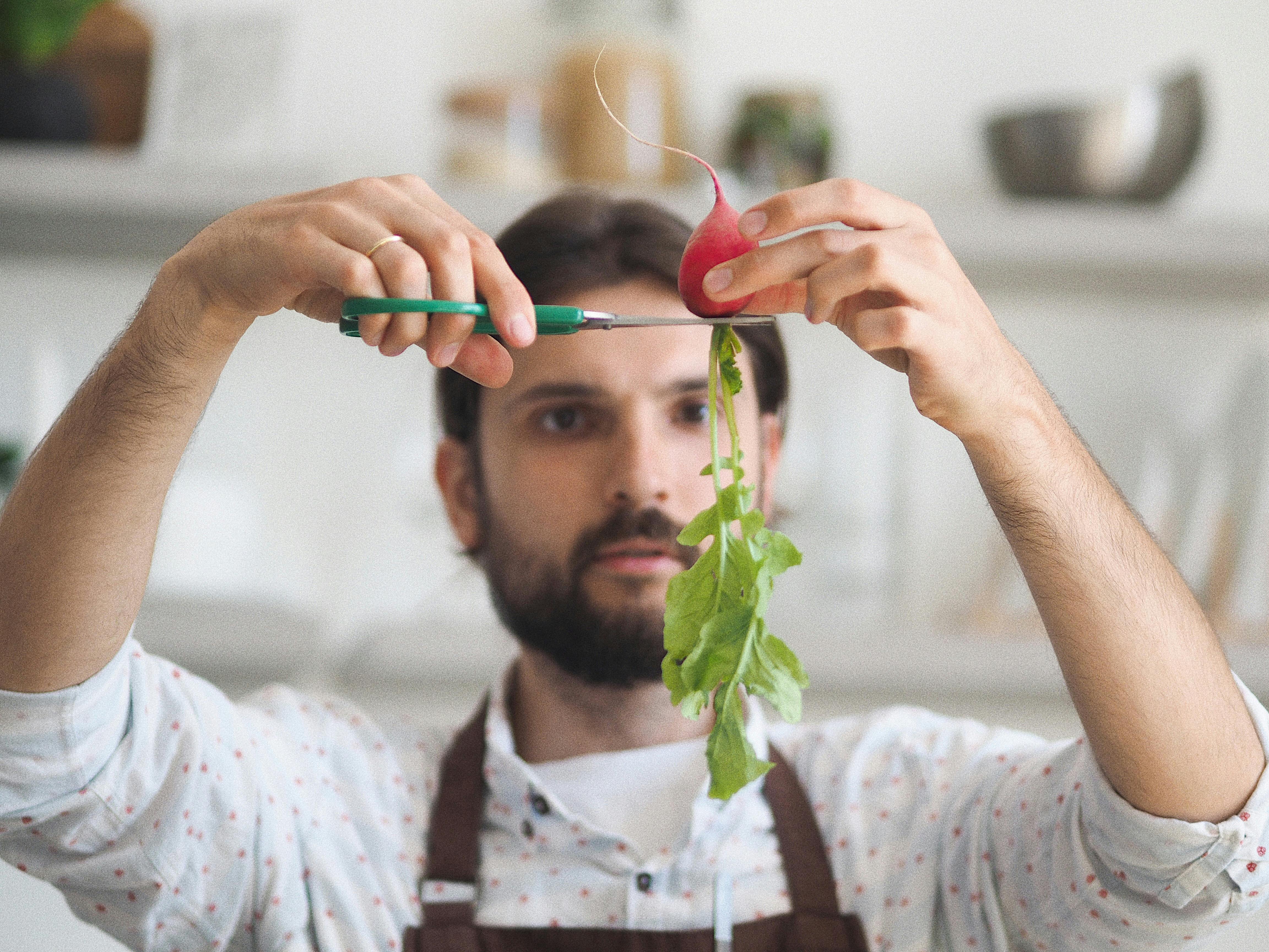 Man skillfully trims a fresh radish in a modern kitchen setting.