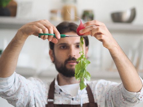 Free Man skillfully trims a fresh radish in a modern kitchen setting. Stock Photo