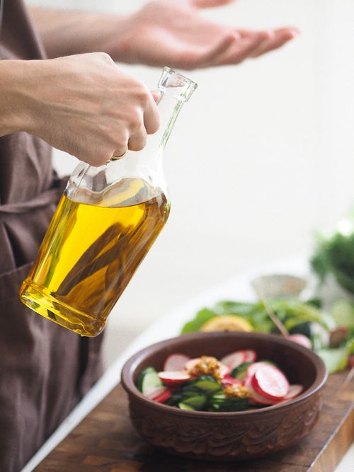 Free A person pours olive oil on a vibrant summer salad with radishes and cucumbers in a rustic bowl. Stock Photo