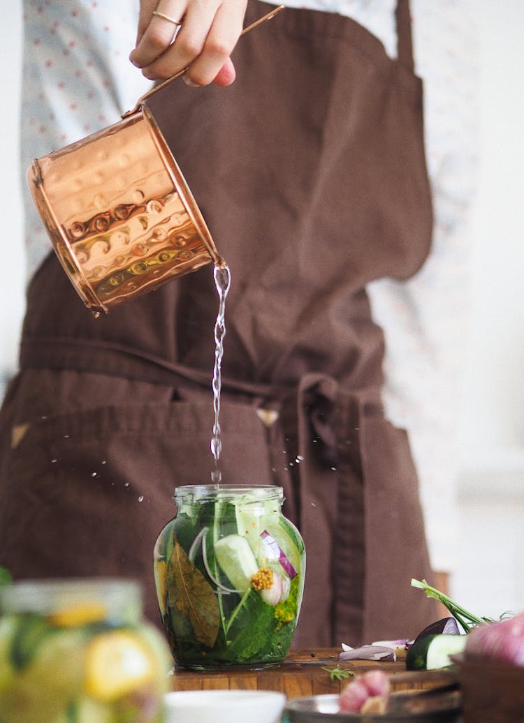 Person Pouring Water In Glass Jar Of Vegetables