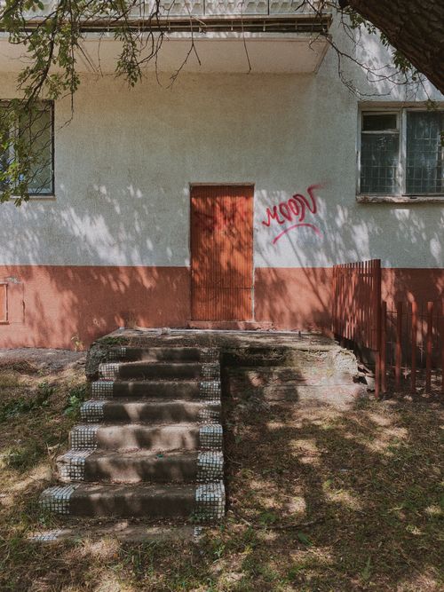 Free Old stairway leading to a graffiti-marked entrance of an abandoned building, shadowed by trees. Stock Photo