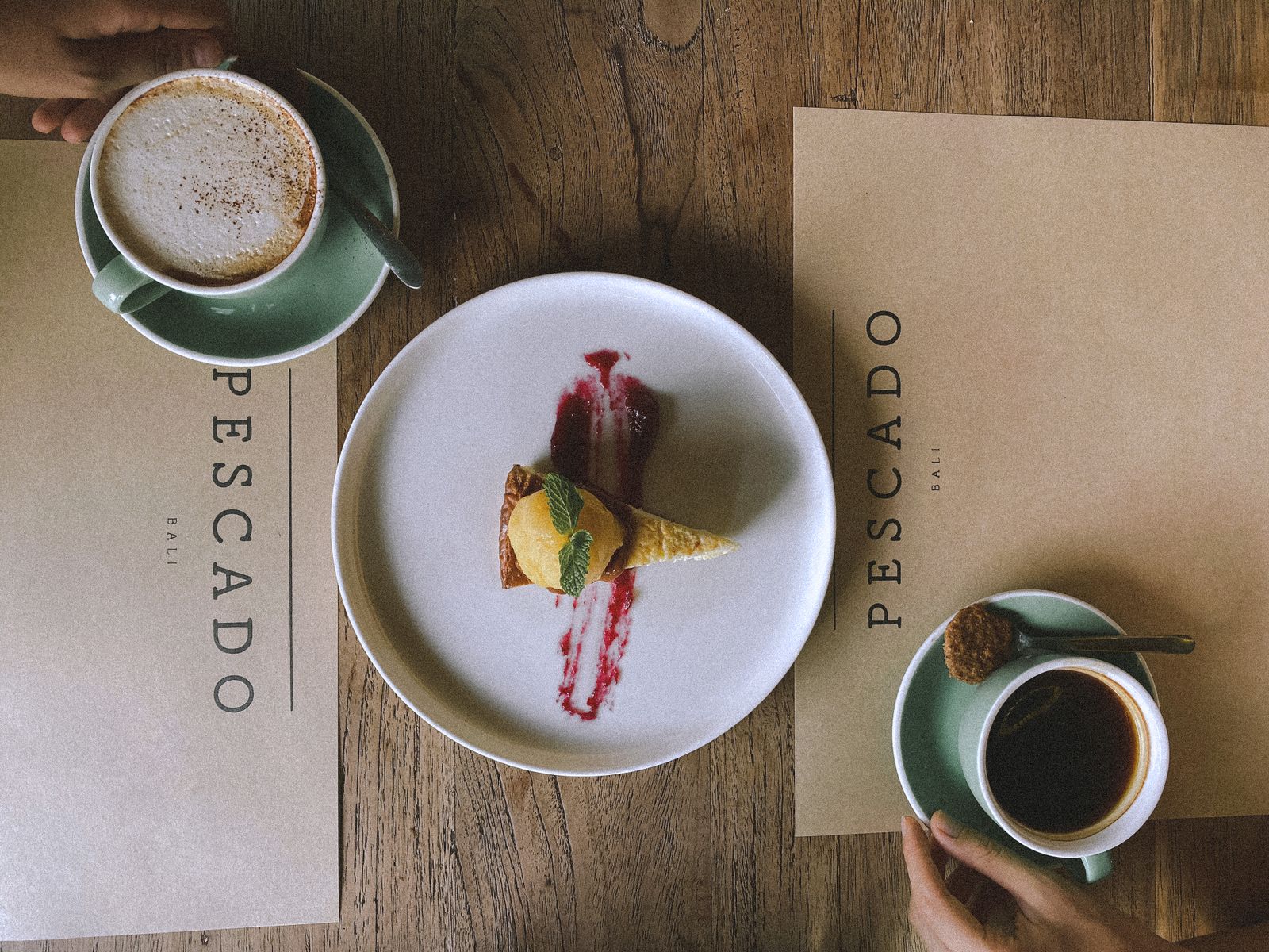 Top view of coffee and dessert setup at Pescado Cafe, featuring cappuccino and cake slice.